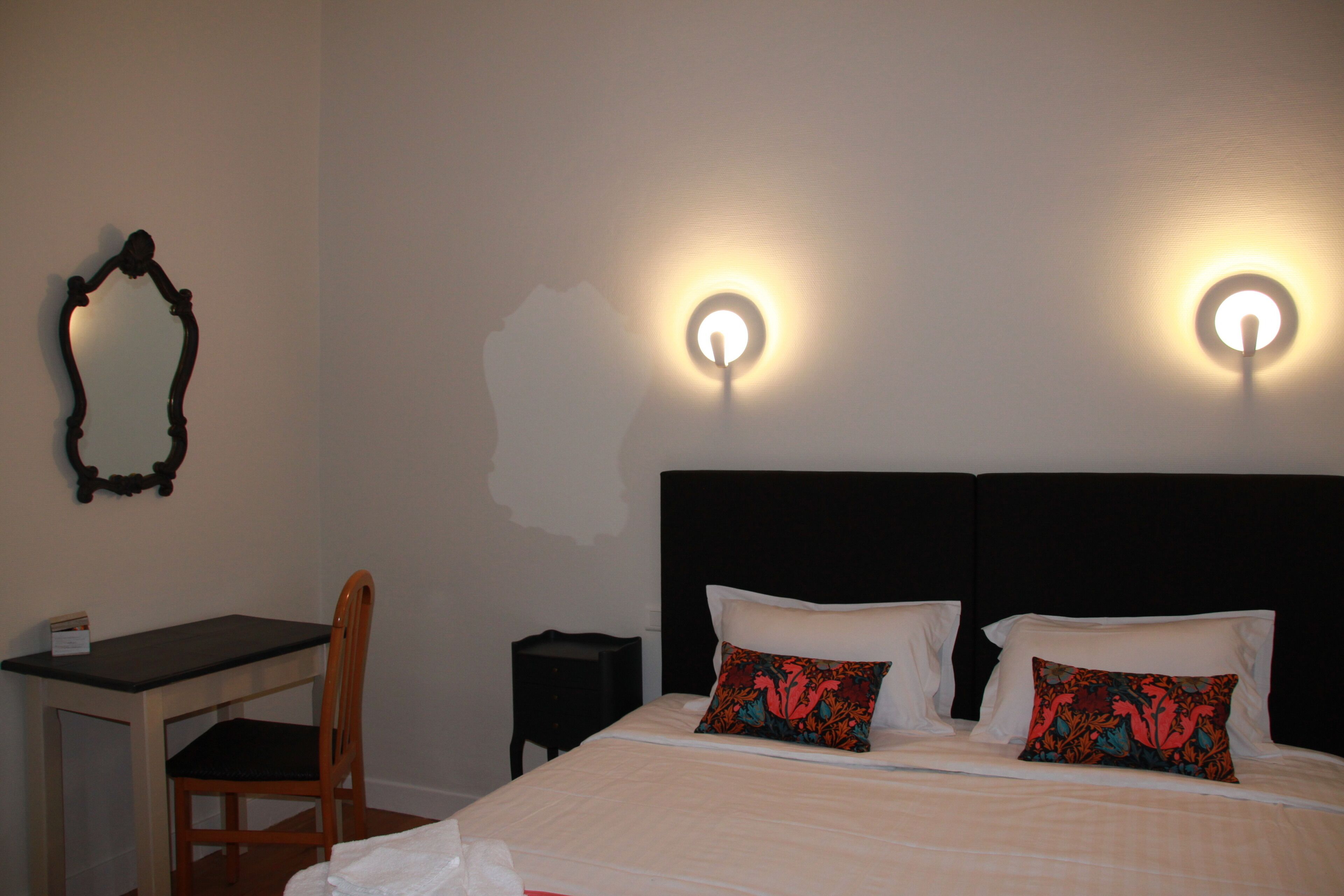 A hotel room with a bed, two pillows, a desk, a chair, and two wall-mounted lights.