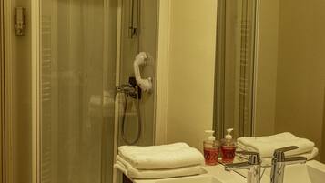 Un baño con cabina de ducha de vidrio, una toalla blanca, dos dispensadores de jabón y un lavabo con grifo cromado.