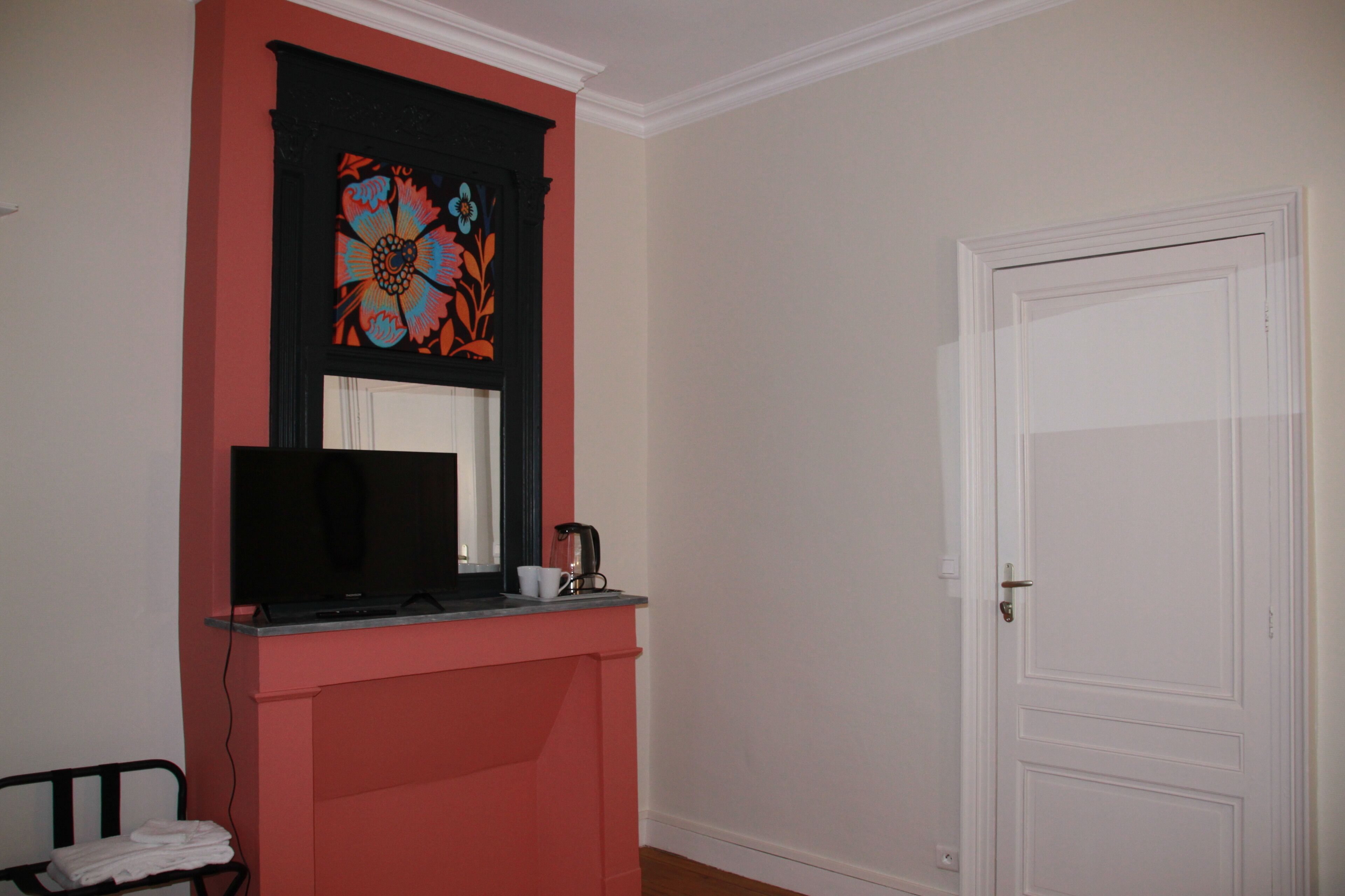 Een kamer met een rode accentmuur, een zwarte televisie op een standaard, een witte deur en een witte muur.