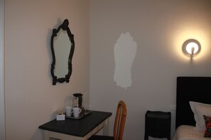 A hotel room with a bed, a desk with a chair, a coffee maker, and a wall-mounted mirror. - La Maison Duffour (Tonneins)