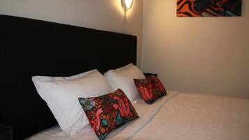 A bed with white and colorful pillows, a black headboard, and a wall-mounted light fixture.
