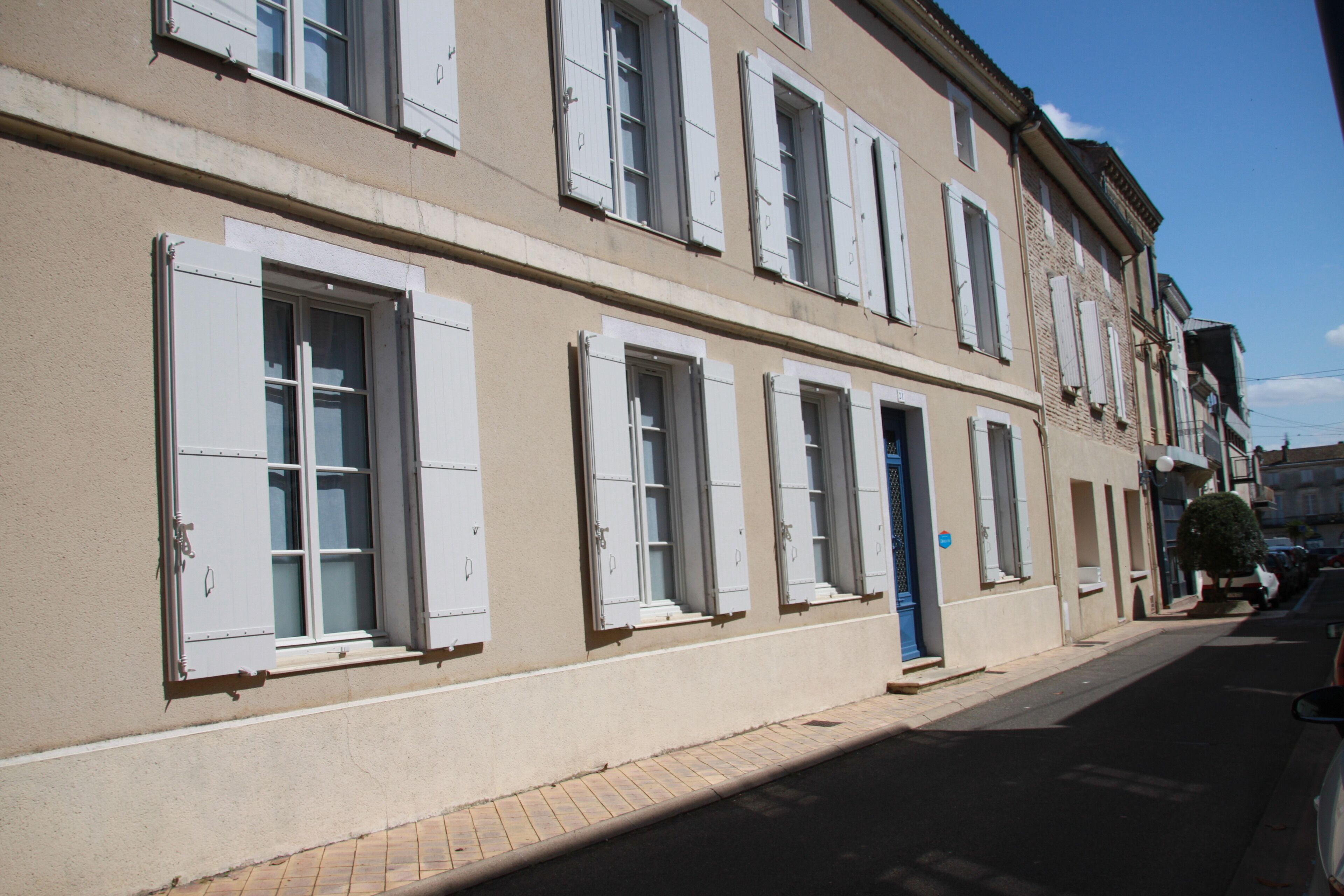 A row of buildings with uniform architecture, featuring multiple windows with shutters, a clean facade, and a paved street.