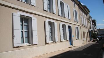 A row of buildings with uniform architecture, featuring multiple windows with shutters, a clean facade, and a paved street.