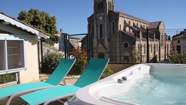 Un jacuzzi con sillones de descanso, una iglesia con campanario y un cielo azul despejado.