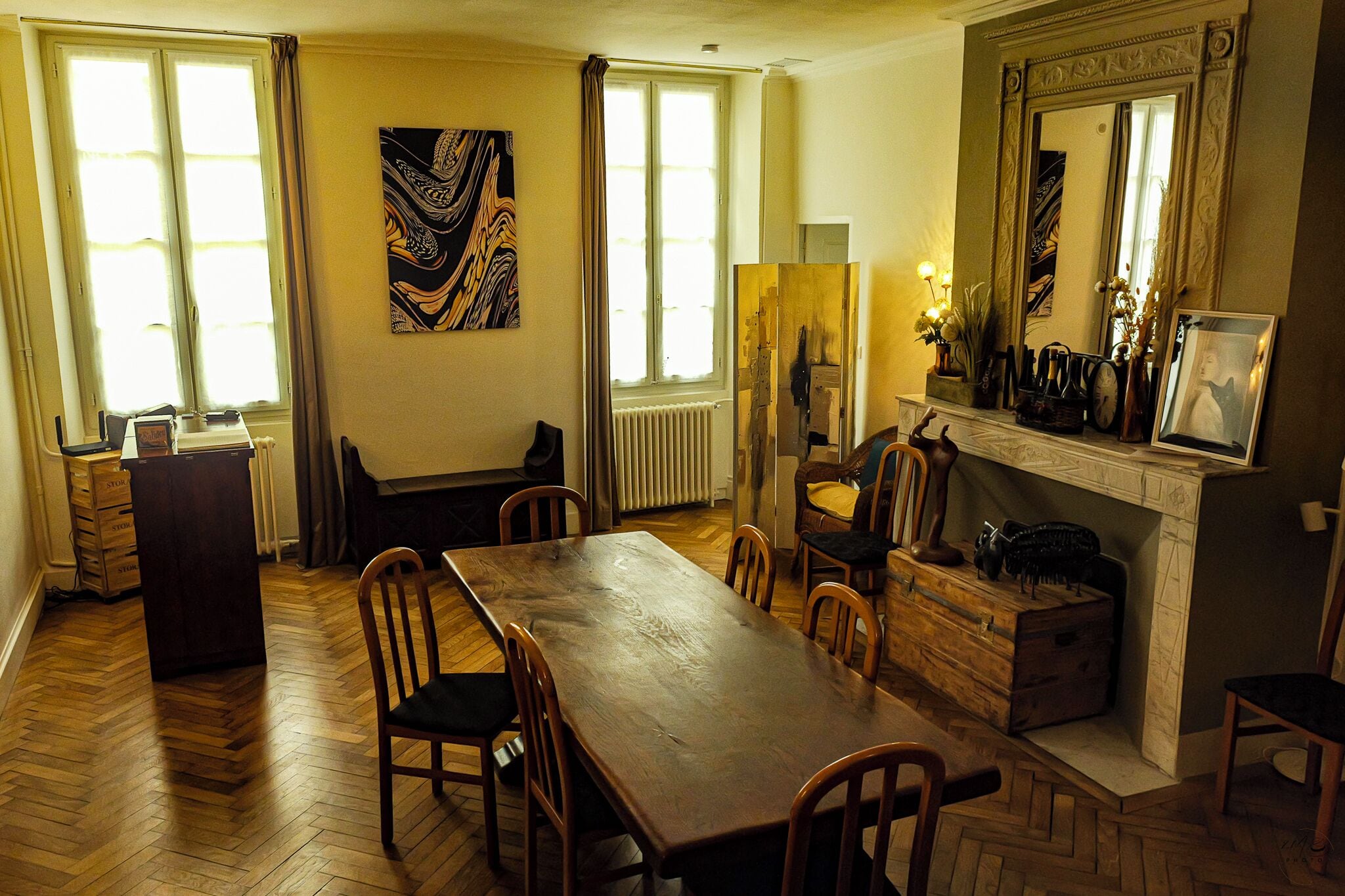A dining area with a long wooden table, chairs, a fireplace, and a large mirror above it.