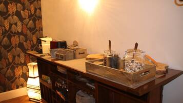 A wooden buffet table with glass jars containing food items, a coffee machine, and a lamp.
