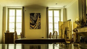 Un salón de conferencias con una larga mesa, sillas, un cuadro en la pared y una ventana con cortinas.
