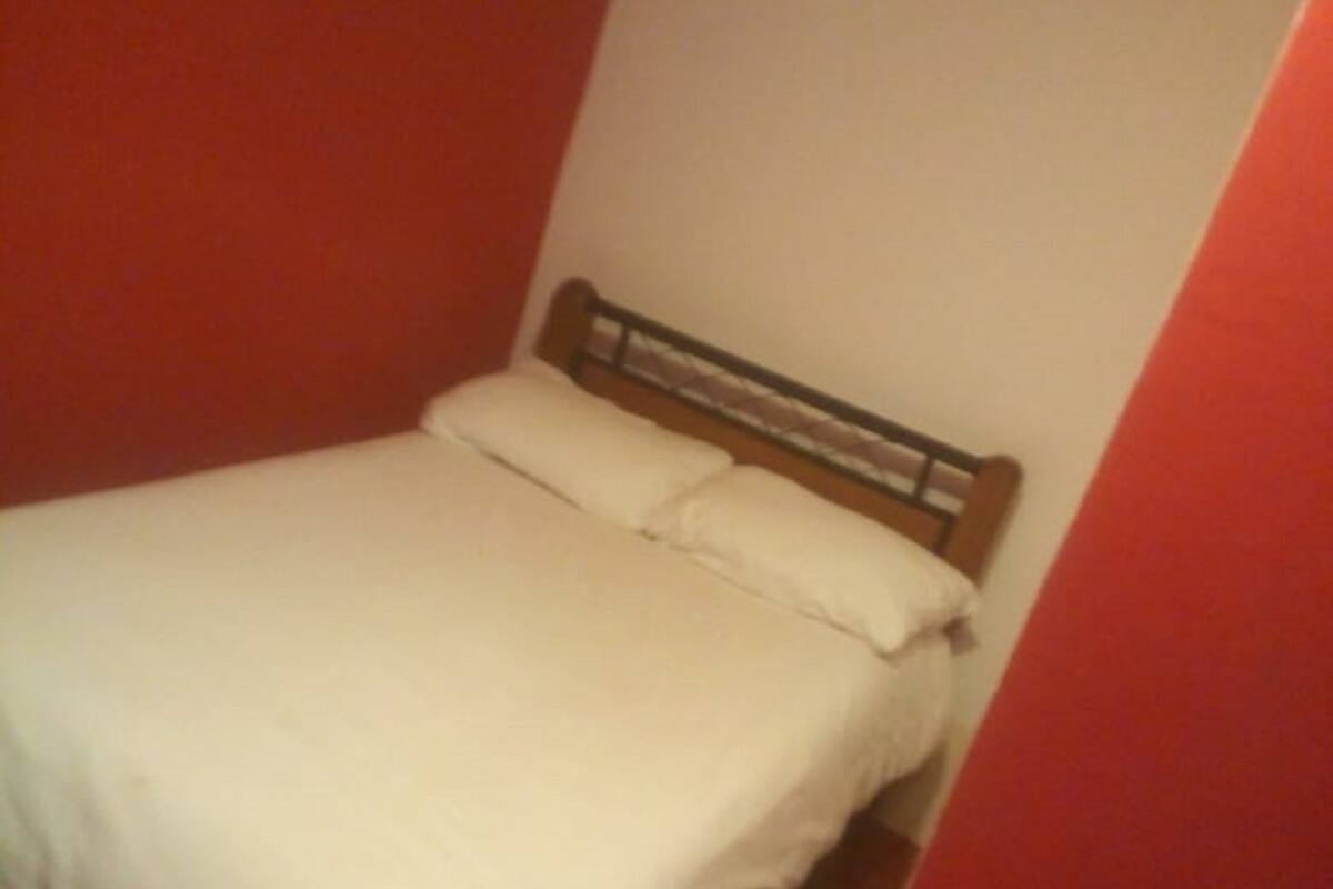 A single bed with white bedding in a room with red walls.