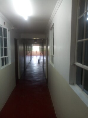 A long, narrow hallway with a red carpet, white walls, and large windows on one side. - Freetown Bar And Restaurant (Nairobi)