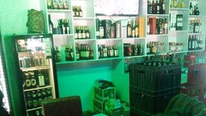 A bar area with shelves stocked with various liquor bottles, a refrigerator with bottles, and a counter with a laptop and papers. - Freetown Bar And Restaurant (Nairobi)