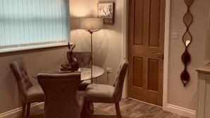 A dining area with a round table and four chairs, a wooden door, and a wall-mounted decorative piece. - Homely luxury cottage 2 (Tantobie)