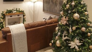 A living room with a brown leather sofa, a Christmas tree, a flat-screen TV, and a fireplace. - Homely luxury cottage 2 (Tantobie)