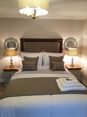 A neatly made bed with a headboard, two bedside tables with lamps, and two wall mirrors.