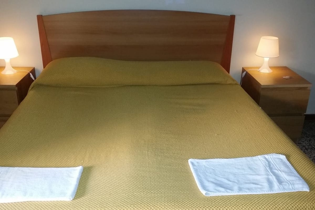 A neatly made bed with a yellow bedspread, two white towels on the bed, and two bedside lamps on wooden nightstands.
