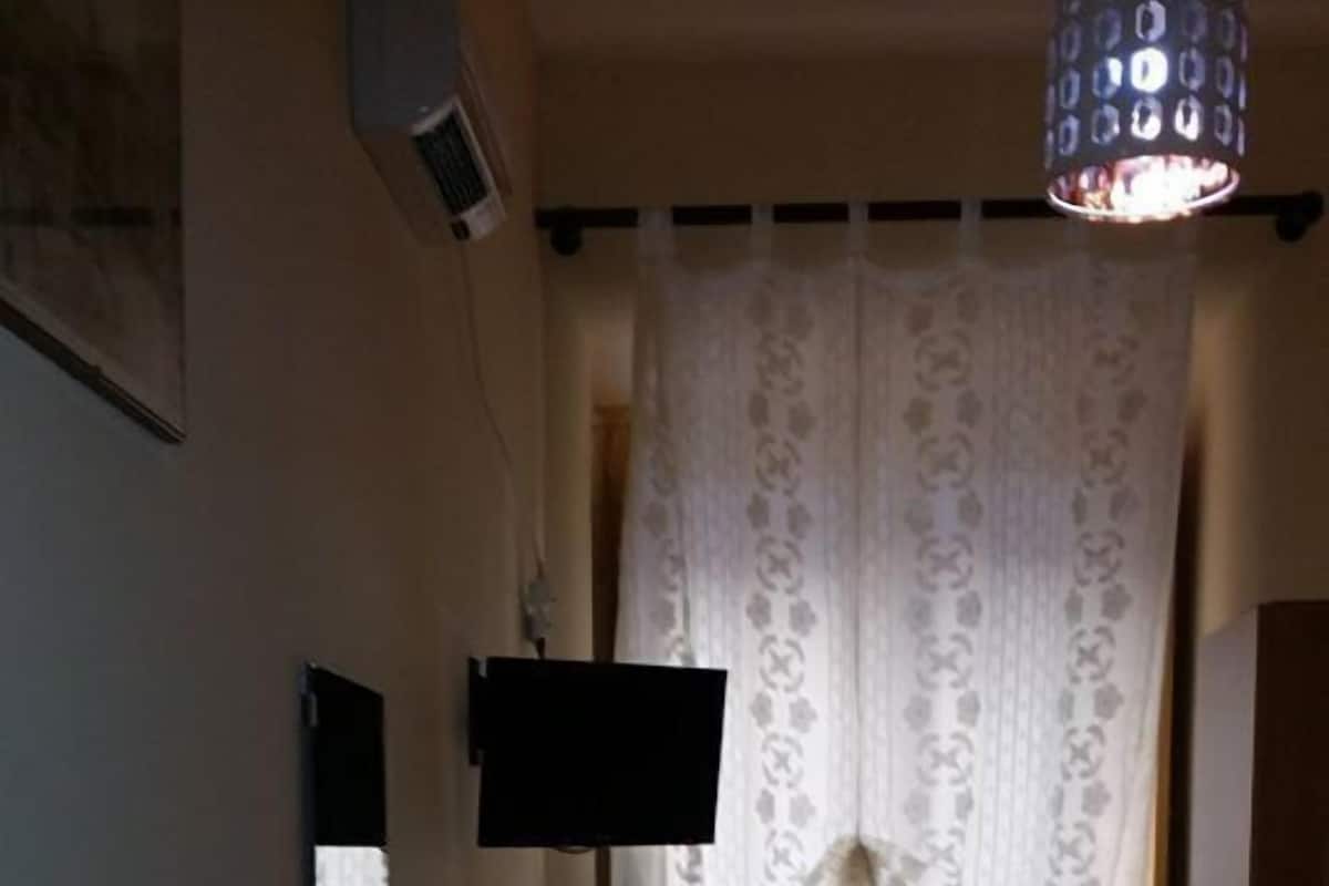 A small dining area with a table and chairs, a TV mounted on the wall, and a patterned curtain.