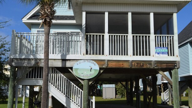 Uma casa de dois andares com varanda, deck de madeira e placa indicando ser propriedade para aluguel.
