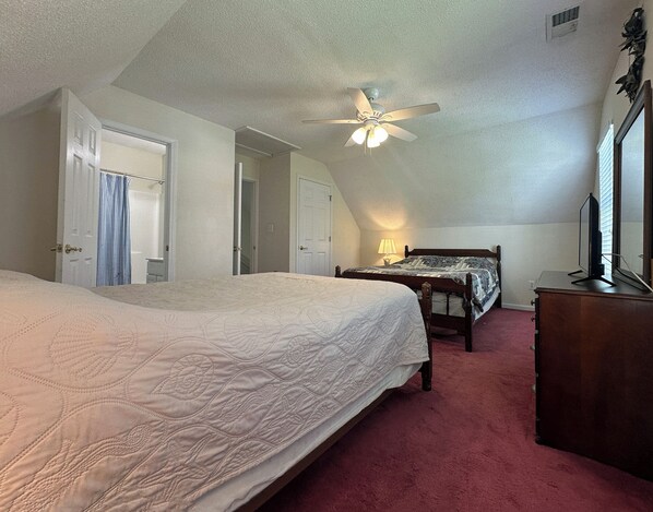 A bedroom with a large bed, a smaller bed, a ceiling fan, a dresser, and a mirror.