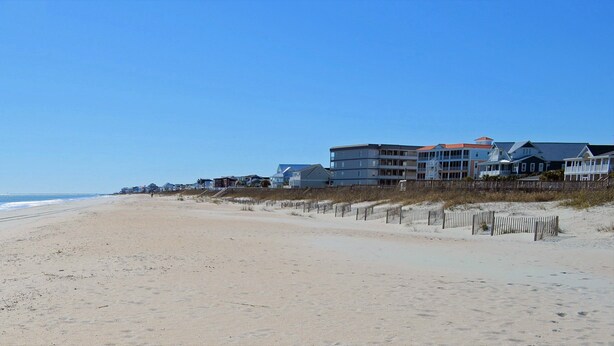 Une plage bordée de maisons donnant sur la mer, un ciel dégagé et une mer calme.