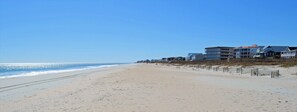 Une plage bordée de maisons donnant sur la mer, un ciel dégagé et une mer calme.