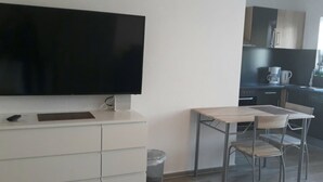 Una cocina moderna con un televisor de pantalla plana, una mesa de comedor con sillas y un cubo de basura.