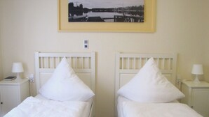 Una habitación de hotel con dos camas individuales, cabeceros blancos, lámparas de noche, una mesita de noche con teléfono y un cuadro en la pared.