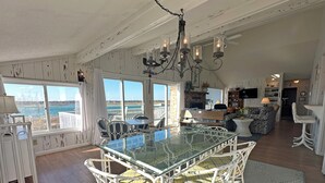Amplia sala de estar con mesa de vidrio para comer, sillas de mimbre blanco y vista al océano.