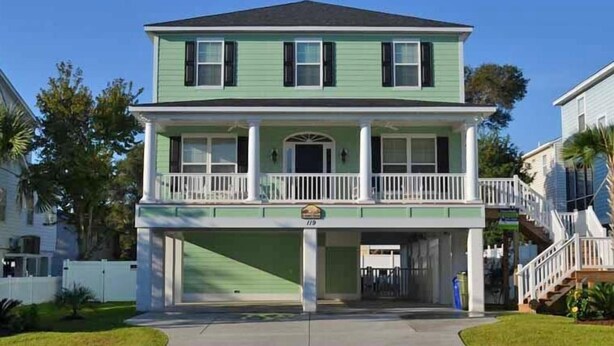 Ein zweistöckiges Haus mit Veranda, Garage und einer Treppe zum zweiten Stock.
