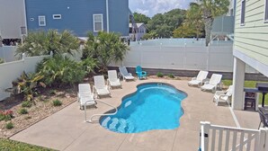 Ein Garten mit Swimmingpool, weißen Liegestühlen und einem weißen Zaun.