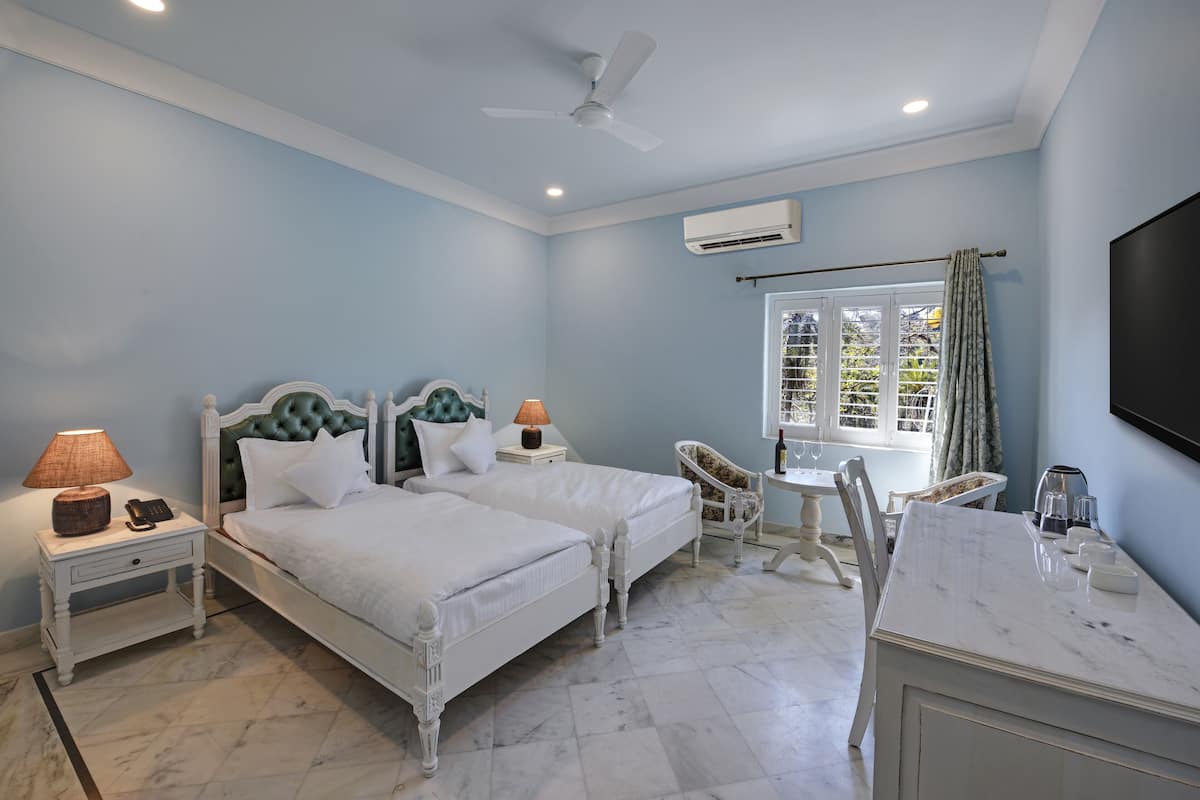 A bedroom with two beds, a desk, a chair, a TV, and an air conditioning unit.