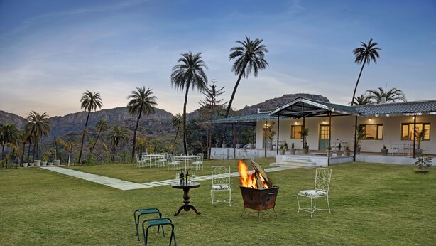 Un espacio exterior bien cuidado con una chimenea, asientos y vistas a palmeras y montañas.
