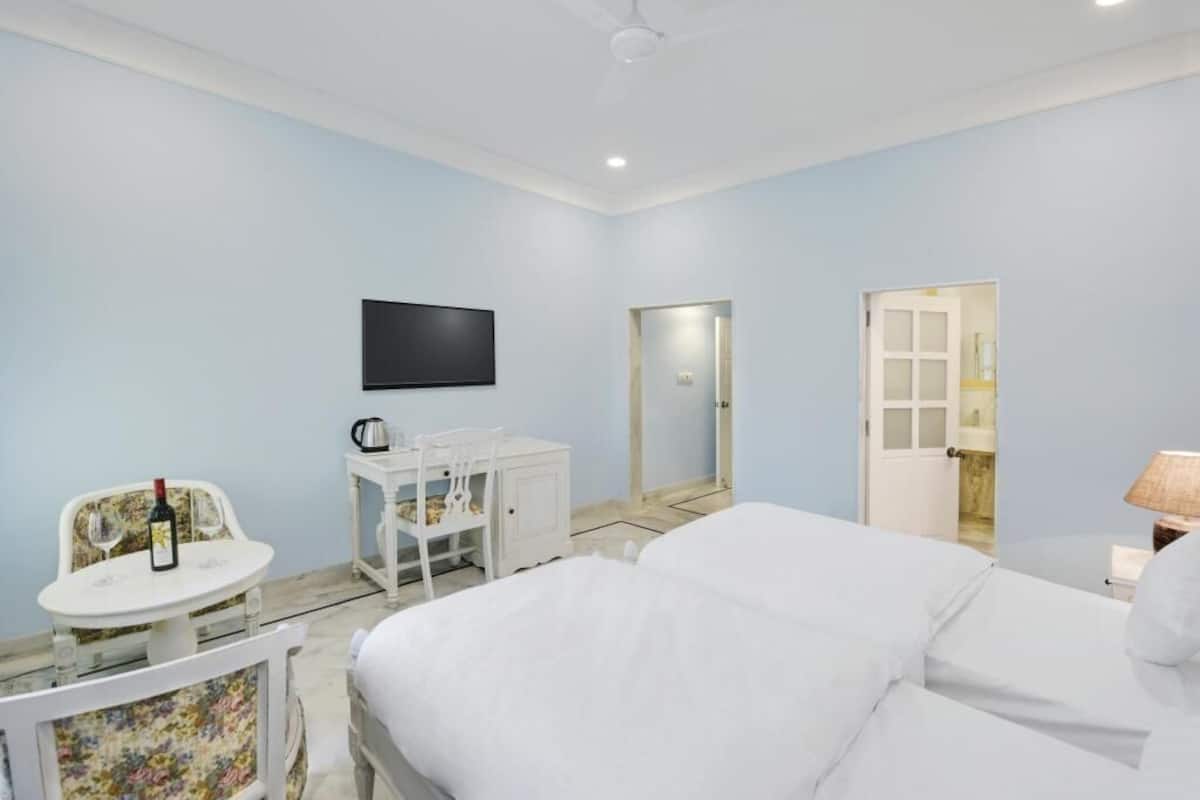 A bedroom with a bed, a TV, a small table with a bottle and glass, and a chair.