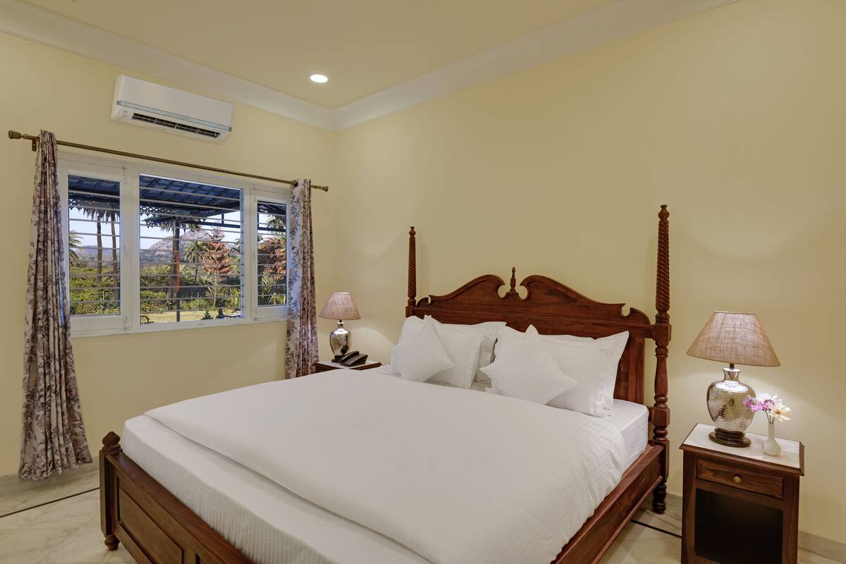 A neatly made bed with a wooden headboard, a bedside table with a lamp, and a window with curtains.