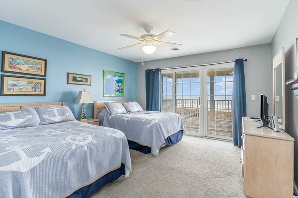 A bedroom with two beds, a ceiling fan, a desk with a computer, and a view of the outdoors through a sliding glass door. - All Aboard - Oceanfront in Garden City Beach (Garden City)