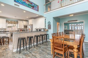 A spacious kitchen with a central island, bar stools, and a dining area with a wooden table and chairs. - All Aboard - Oceanfront in Garden City Beach (Garden City)