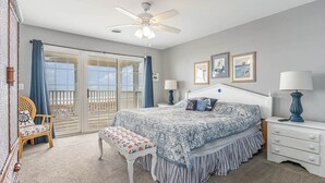 A bedroom with a bed, a bench, a nightstand, a ceiling fan, and a view of the outdoors. - All Aboard - Oceanfront in Garden City Beach (Garden City)