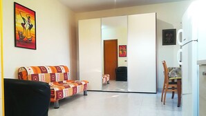 A living room with a sofa, a dining table with chairs, a refrigerator, and a sliding door leading to another room. - Near The Beach And The Center Of Otranto - Apartment Eleonora 5 Places (Otranto)