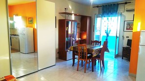 A compact kitchen with a refrigerator, stove, and cabinets. There is a dining area with a table and chairs, and a sliding door leading to a balcony. - Near The Beach And The Center Of Otranto - Apartment Eleonora 5 Places (Otranto)