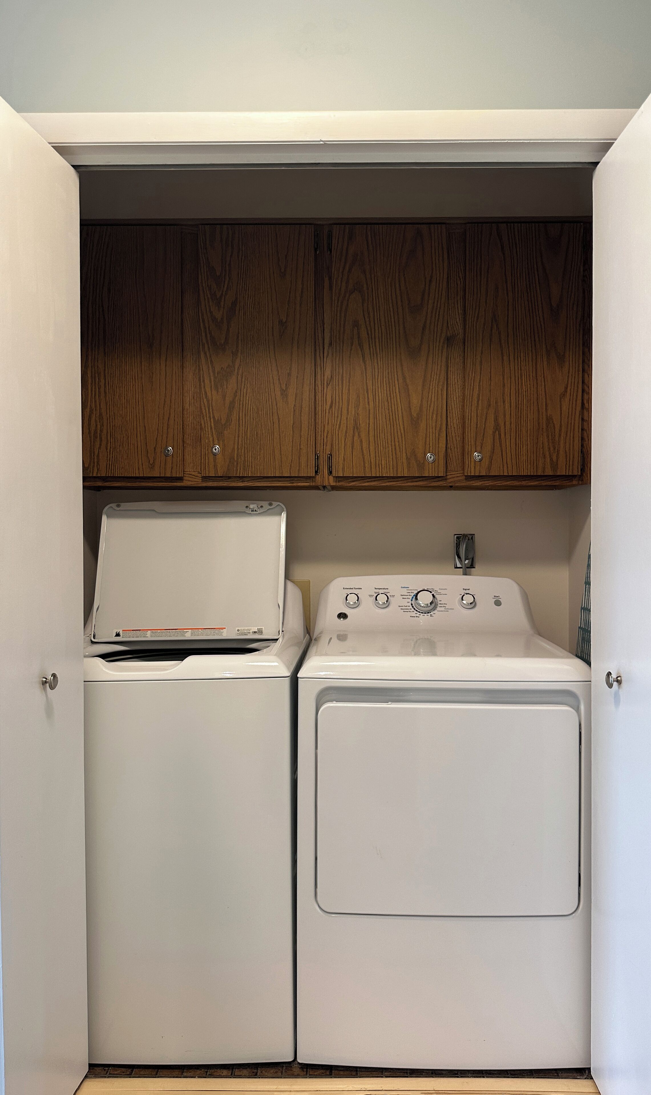 A compact laundry area with a washing machine and dryer, wooden cabinets above, and a small countertop.