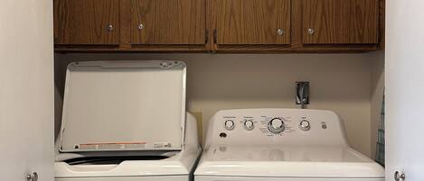 A compact laundry area with a washing machine and dryer, wooden cabinets above, and a small countertop.