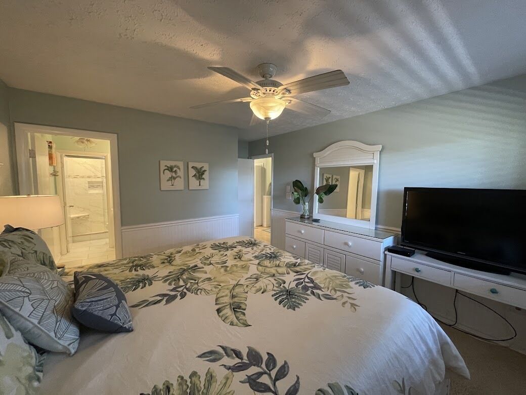 A bedroom with a bed, a ceiling fan, a television, and a dresser.