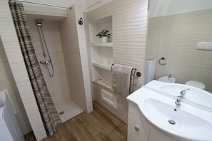 Casa de banho com chuveiro, lavatório, sanita e porta-toalhas.