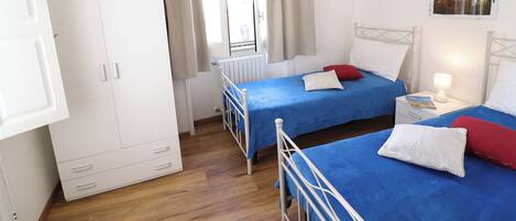 Une chambre avec deux lits, une armoire, une fenêtre avec des rideaux et un tableau au mur.