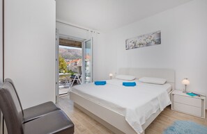 Un dormitorio con una cama, una silla, una mesita de noche, una lámpara y un cuadro en la pared.