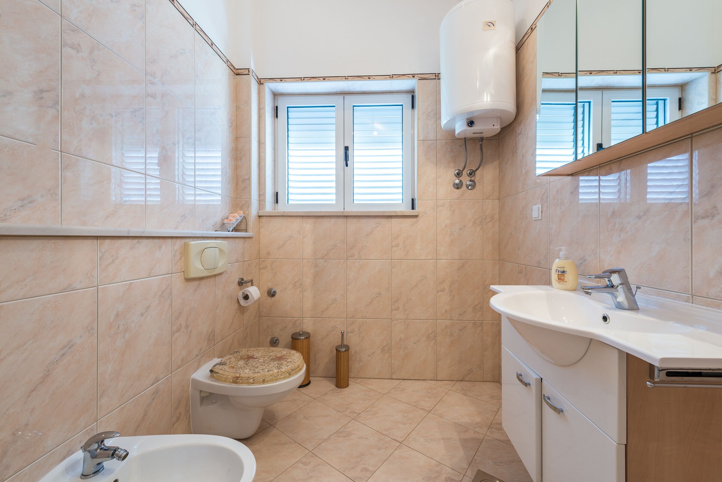 Un baño con inodoro, bidé, bañera, lavamanos y ventana con persianas.