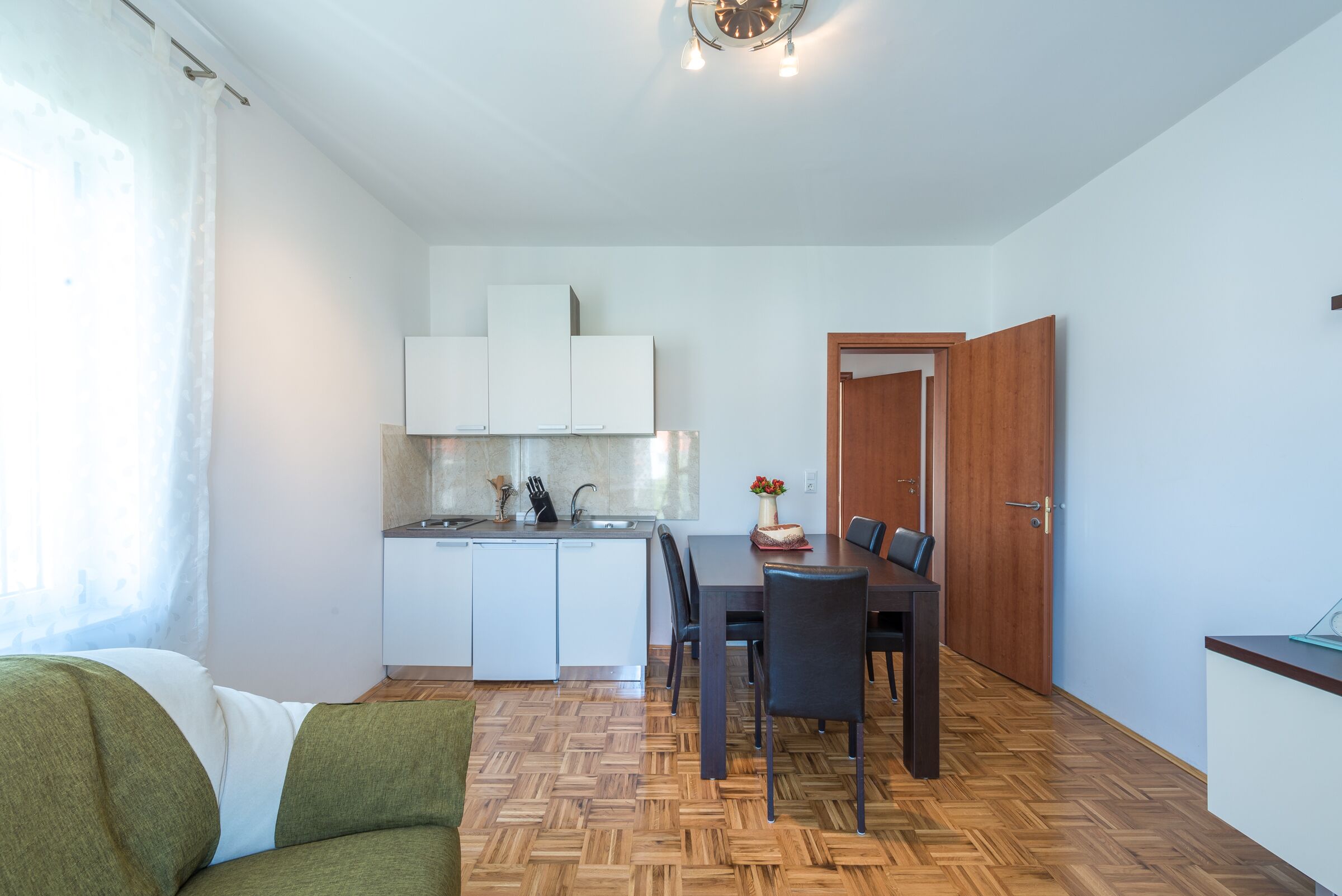 A compact living space with a kitchenette, dining area, and a wooden herringbone floor.