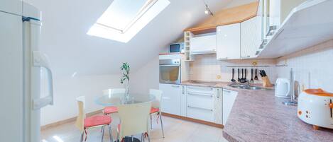 A modern kitchen with a skylight, white cabinets, a dining area with a glass table and chairs, and a countertop with a toaster.