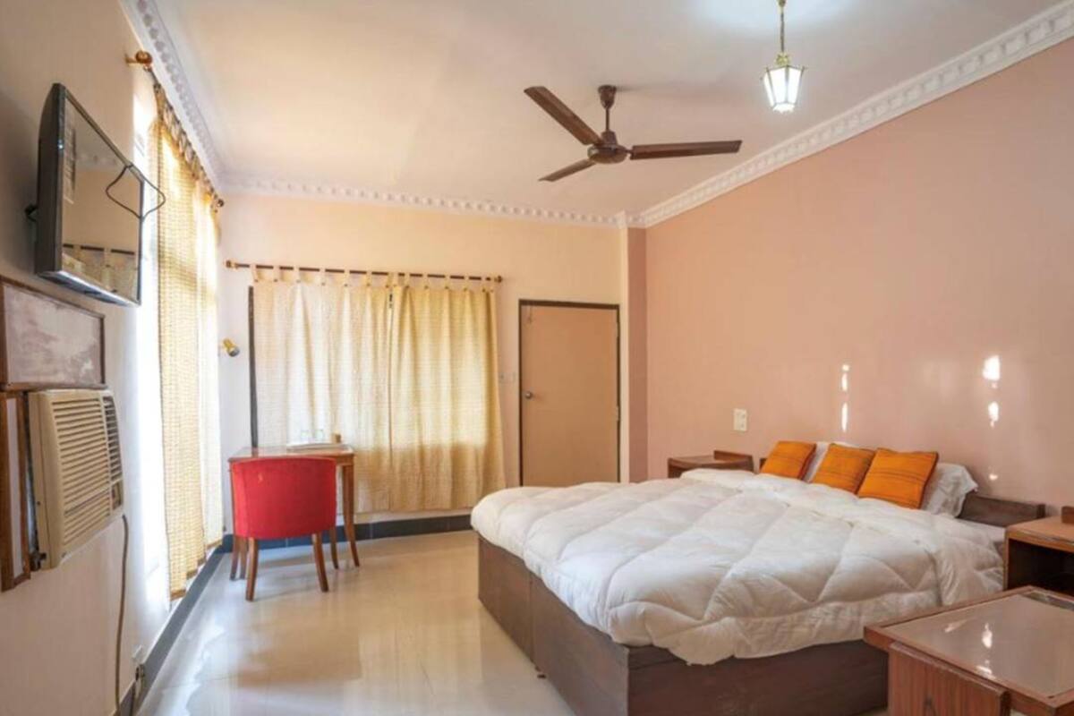 Un dormitorio con una cama, un escritorio, una silla, un ventilador de techo y una puerta.