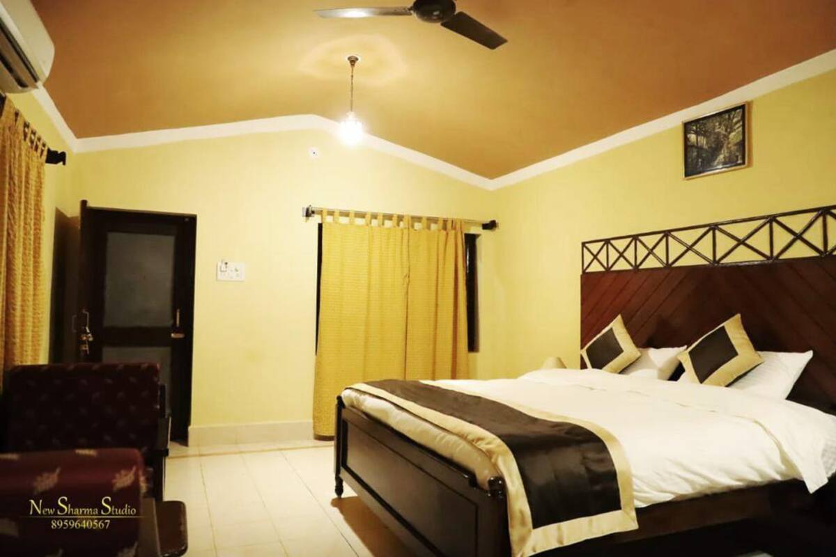 Habitación de hotel con cama, ventilador de techo, televisor y ventana con cortinas.