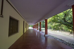 A covered corridor with red pillars and a tiled floor, leading to a natural outdoor area. - Maharaja Kothi (Manpur)
