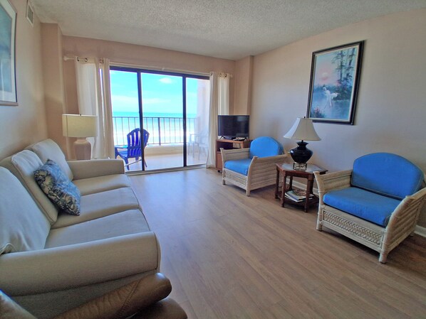 A living room with a sofa, two armchairs, a TV, and a table. There is a balcony with a view of the beach. - Atalaya Towers 103 - Oceanfront in Garden City Beach (Garden City)